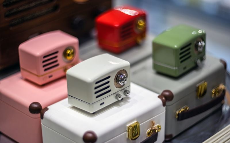 Four small, colorful radios in baby pink, white, bright red and forest green playing oldies